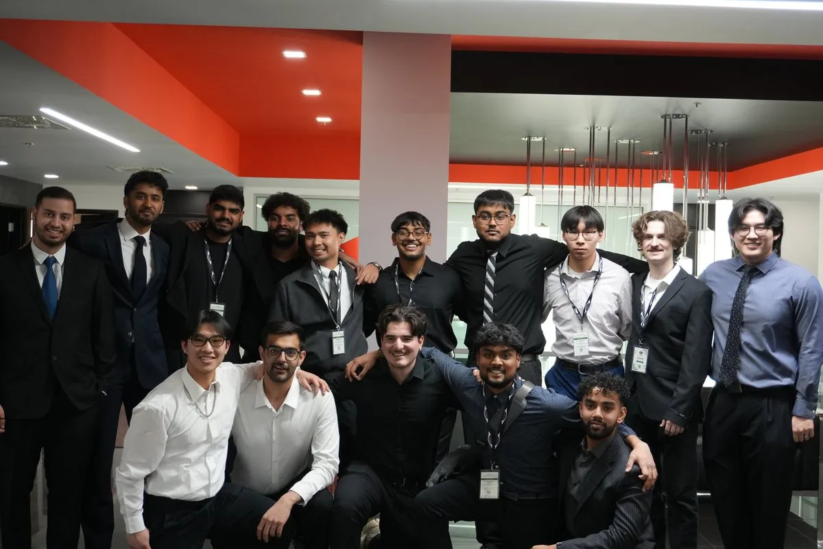 A large group of students in suits and dress shirts poses together in a lobby, some kneeling in front.
