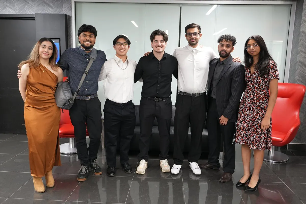 Seven students in formal wear stand arm in arm in a lobby.