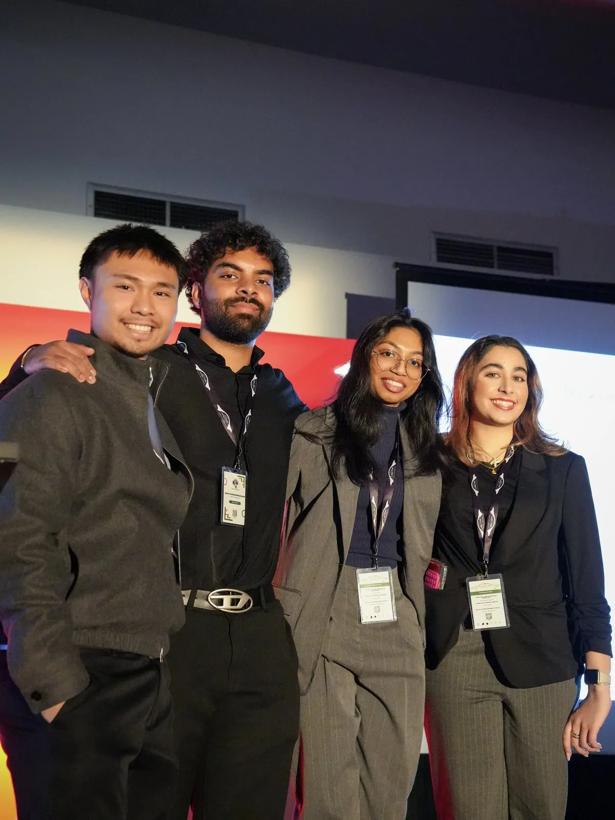 Four students in business attire pose arm in arm on a stage.