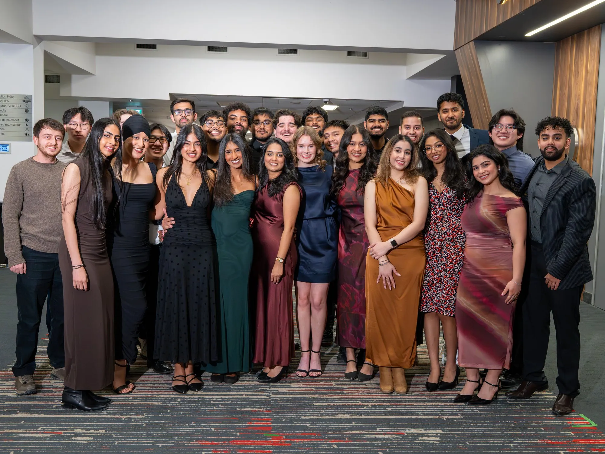 A large group of students in formal attire posing together in a conference hallway.