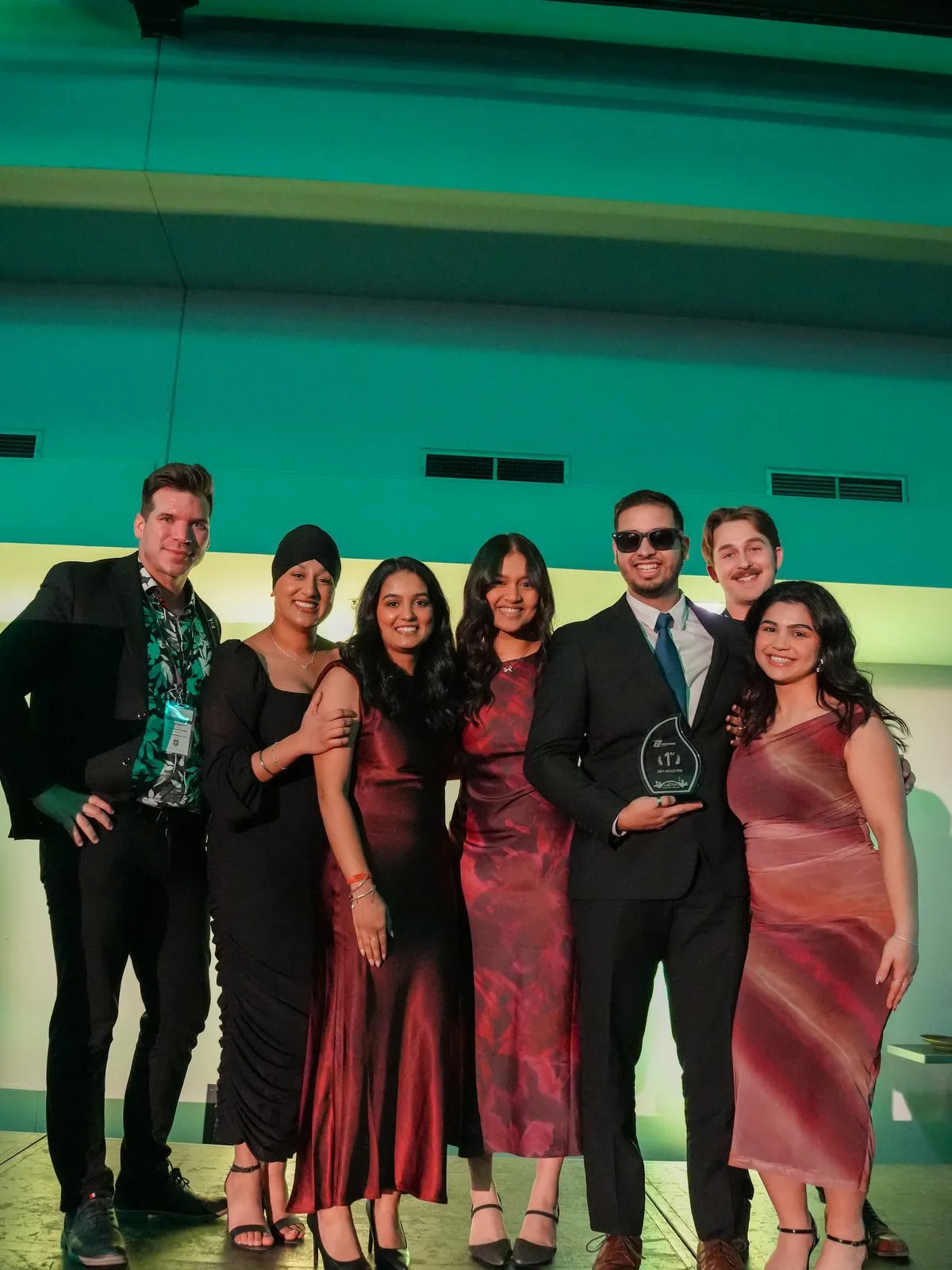 Seven people in formal wear pose on a stage; one holds a glass trophy reading '1er Défi Industrie'.